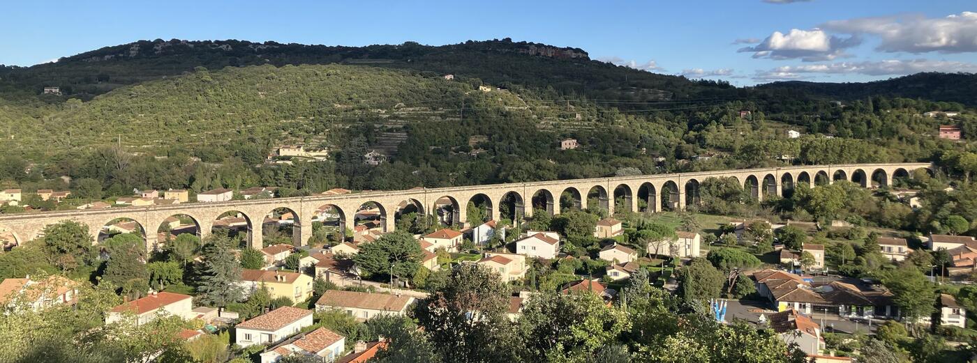 Bédarieux vue depuis les hauteurs : le viaduc ferroviaire traverse toute la vallée, le village s'étend en contrebas, les collines boisées du Haut-Languedoc ferment l'horizon.